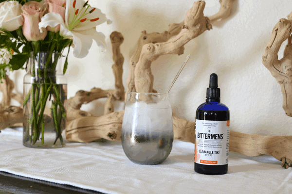 A stemless wine glass on a table with a bottle of bitters next to it. 