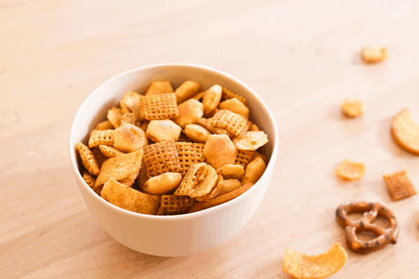Small bowl of homemade Chex Mix on a wooden cutting board. 
