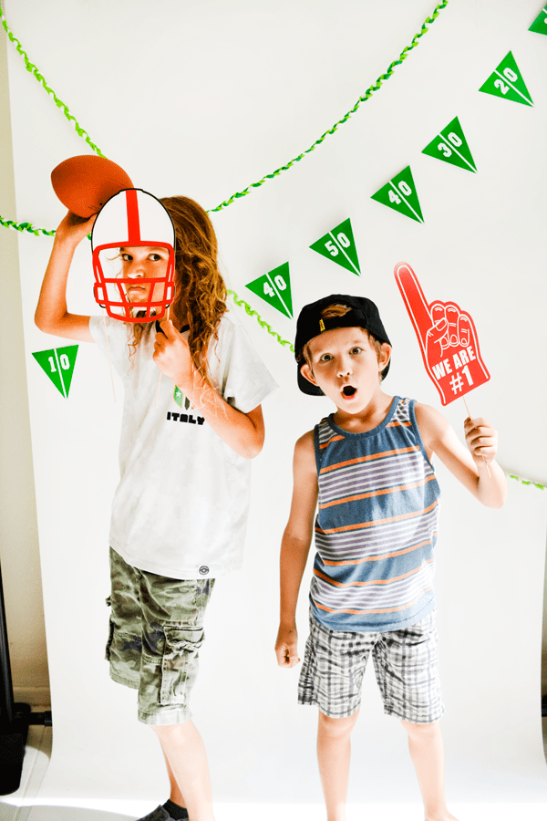 Two kids with football party props in front of a photo backdrop. 