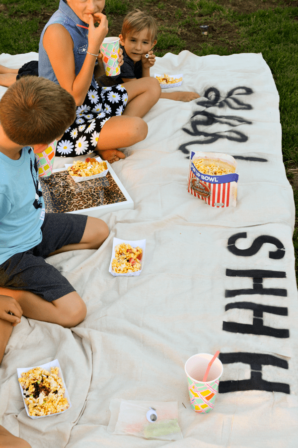 Kids sitting on a blanket and eating popcorn for a backyard movie party.