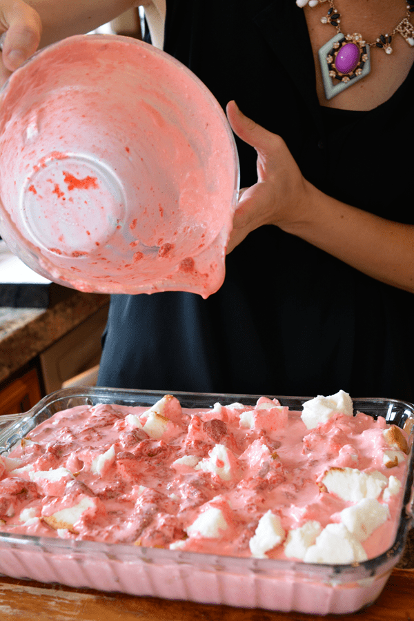 Pouring strawberry jello and Cool Whip over angel food cake. 