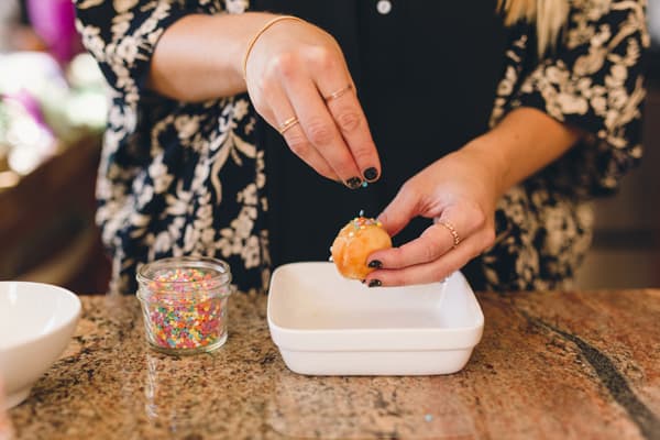 Woman adding sprinkles to a donut hole. 