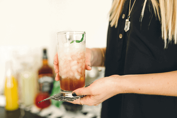 Woman holding a tall glass with a Bourbon cocktail with champagne.