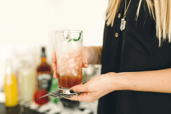 Woman holding a tall glass with a Bourbon cocktail with champagne. 