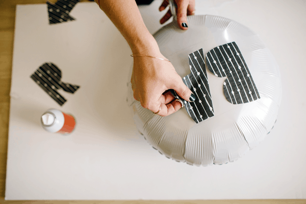 A girl making a sign for a party by glueing letters to a helium balloon. 