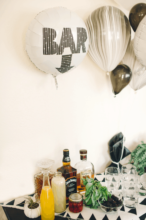 A white mylar balloon with the word "bar" on it in black and white letters near a bar for a party. 