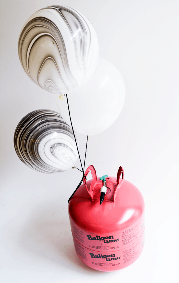 A Balloon Time Helium Tank with black and white marble balloons tied to it. 