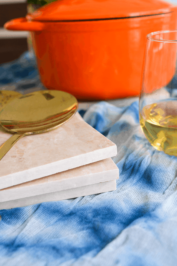 A close up of a stack of tile trivets on a table with a serving spoon laying on top with a glass of wine next to it. 