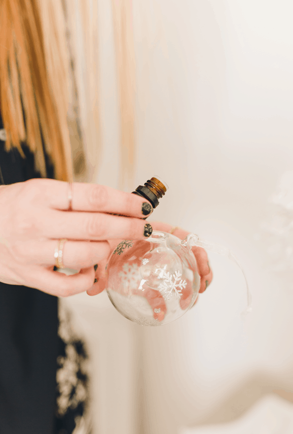 Person holding a glass ornament and adding essential oils to it. 