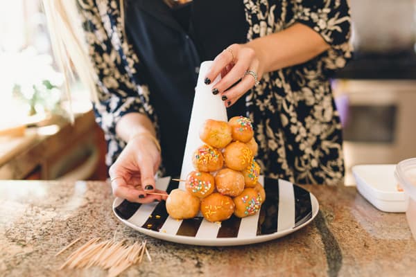 Woman adding donut holes to a styrofoam tower with toothpicks. 
