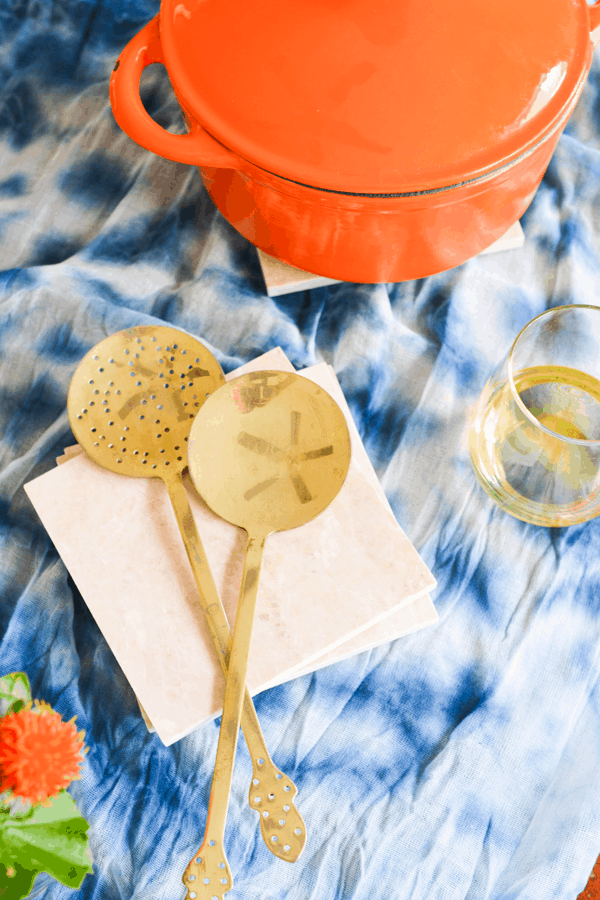 Overhead shot of tile trivets stacked up with utensils on top next to a baking dish and a glass of wine. 