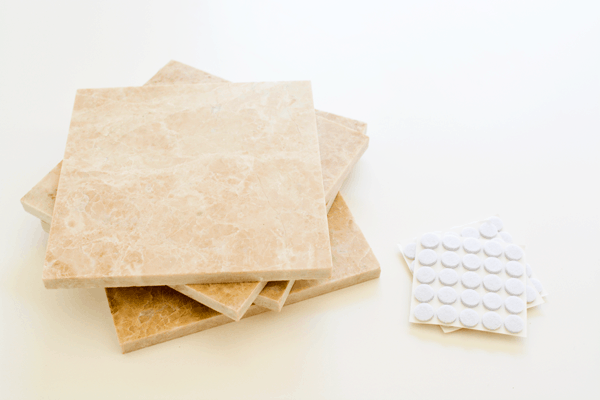 A stack of tile squares on a table next to self-adhesive felt protective tabs.