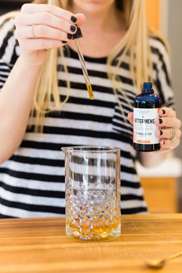 Woman adding drops of bitters to a cocktail. 