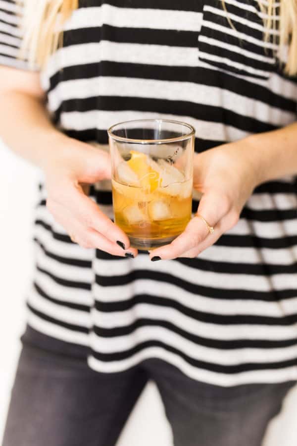 Woman holding a Pine Old Fashioned with an orange twist garnish in her hands. 