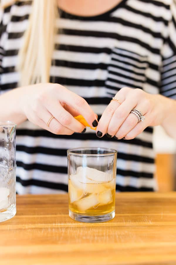 Woman squeezing an orange twist over a Pine Old Fashioned in a cocktail glass. 
