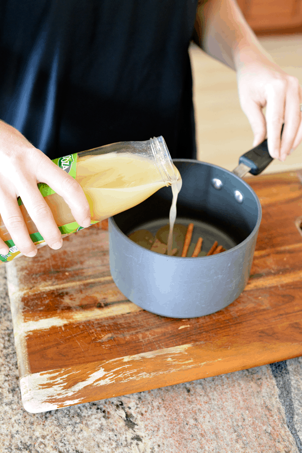 Woman pouring pear juice into a saucepan with cinnamon sticks and cardamom.