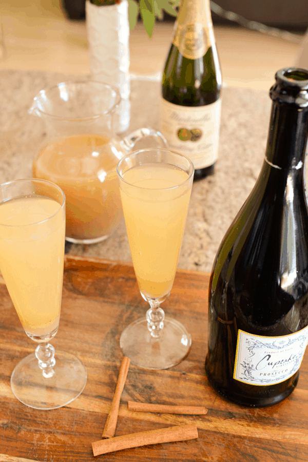 Champagne flutes holding a pear bellini on a table next to cinnamon sticks and a bottle of champagne. 