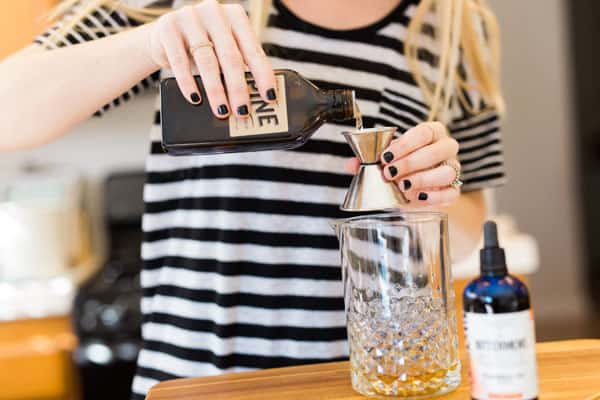 Woman measuring pine syrup in a cocktail jigger. 