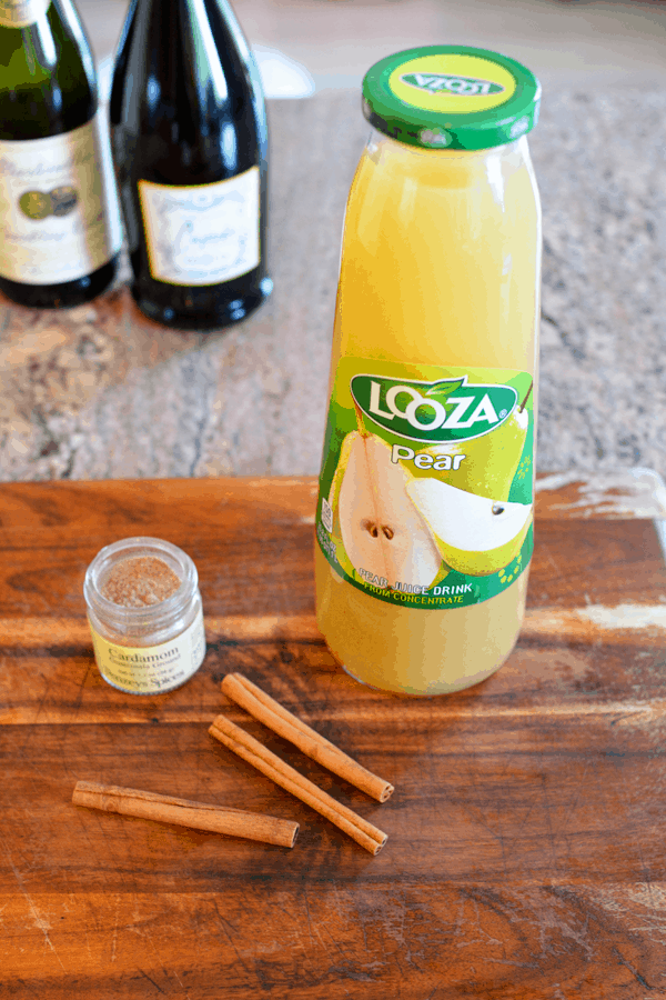 A close up of a bottle of pear juice on a wooden table next to cardamom and cinnamon sticks. 