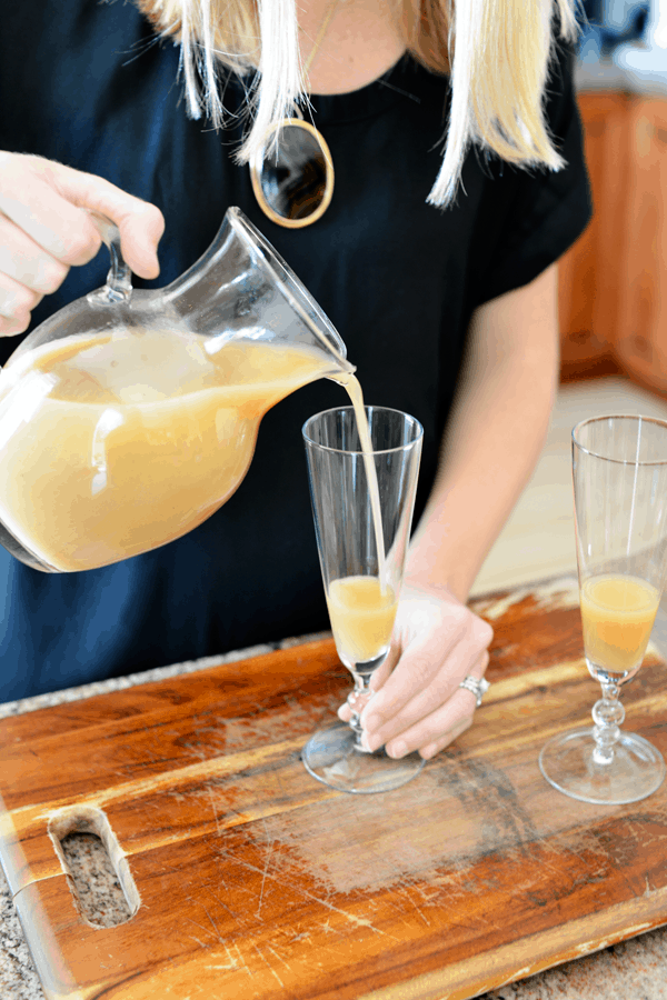 Woman pouring spiced pear juice into champagne flute to make a pear bellini. 