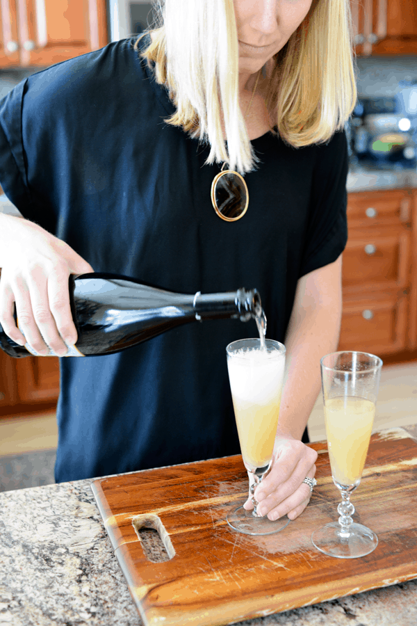 Woman pouring champagne into champagne flutes filled with juice. 