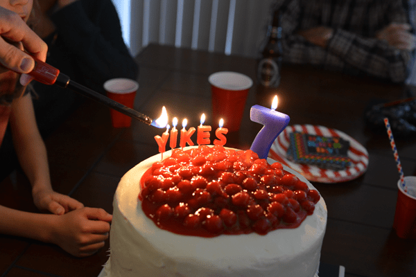 The top of a white frosted cake with cherry pie filling and candles that spell out "yikes" and a number "7".