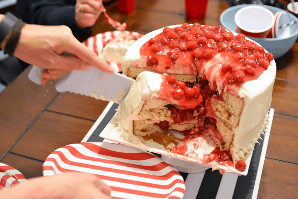 A person cutting a layered vanilla cake with cherry pie filling baked in.