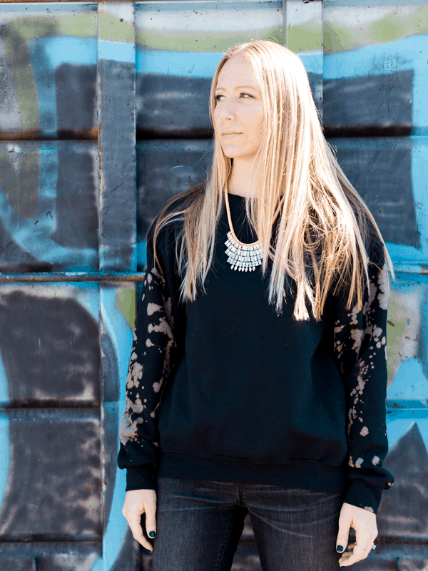 Girl wearing a DIY bleached sweatshirt that is black with areas where the bleach has removed the color. 