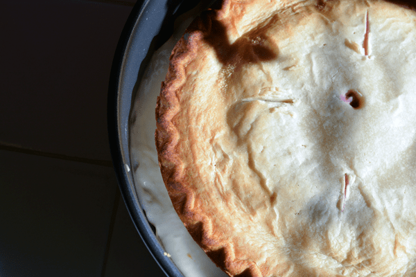 An overhead view of a cake pan with cake batter and a baked pie on top of the batter. 