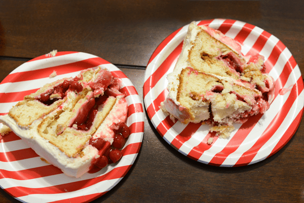 2 pieces of cake with cherry pie filling on red and white striped plates. 