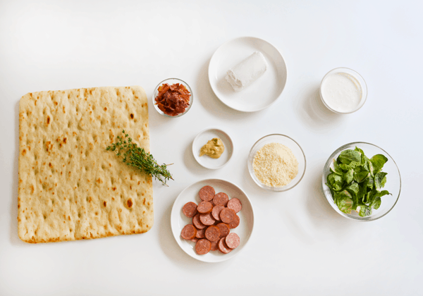 Ingredients to make a goat cheese pizza on a white countertop.