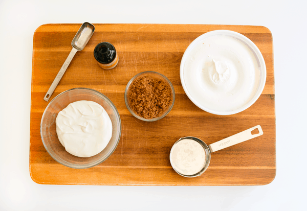 Ingredients to make strawberries romanoff dip on a wooden cutting board.