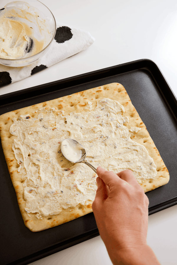 A woman spreading a mixture of goat cheese and cream on a pizza crust on top of a baking sheet.