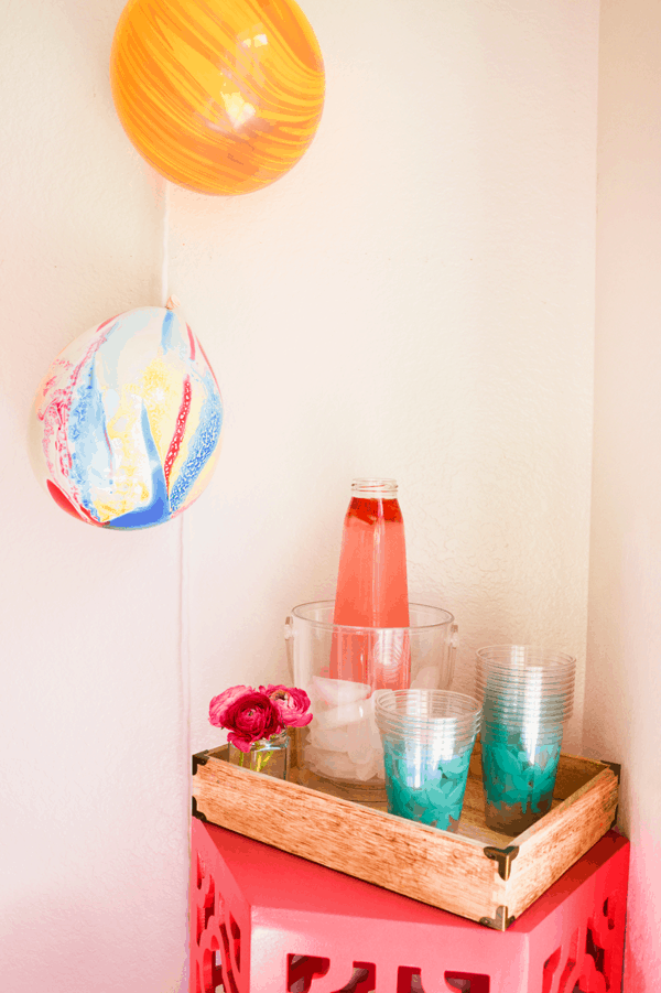 Pink table with wood tray holding plastic party cups and an ice bucket with strawberry lemonade for an easy dinner party.