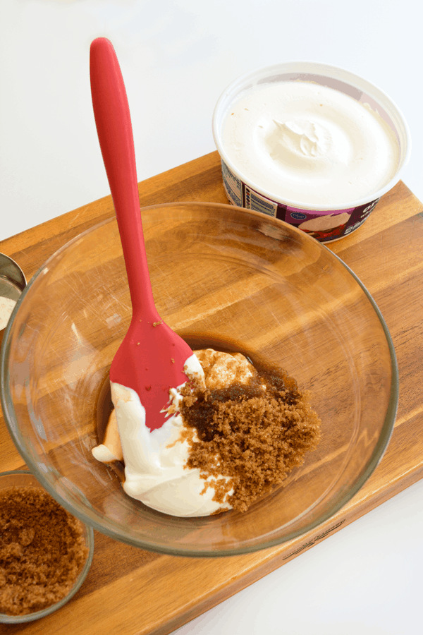A bowl filled with sour cream, brown sugar and vanilla being mixed with a spatula.