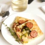 Two slices of goat cheese pizza on a white plate next to a sprig of thyme.