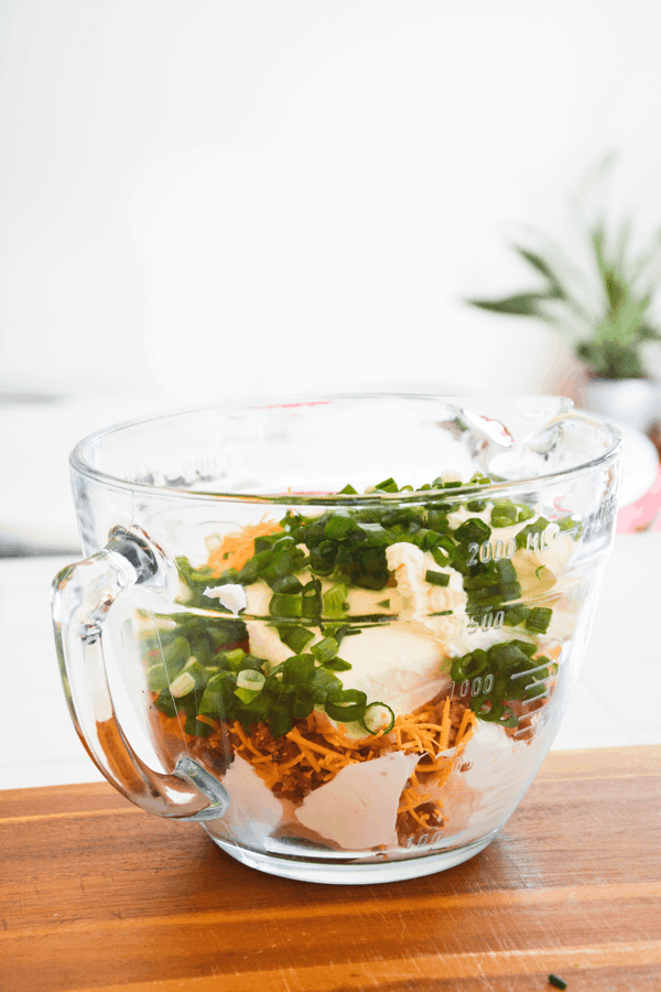 Mixing bowl with ingredients like cheese, sour cream and green onions in it. 