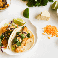 Easy fish stick tacos surrounded by fresh ingredients like cheese and fresh herbs.