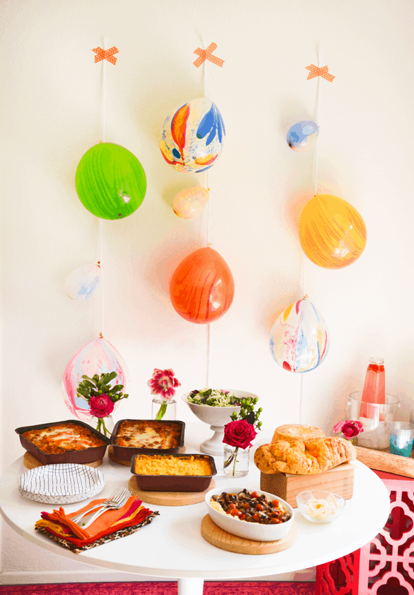 A table set with food for a party next to a wall with colorful balloons taped up as a decoration.