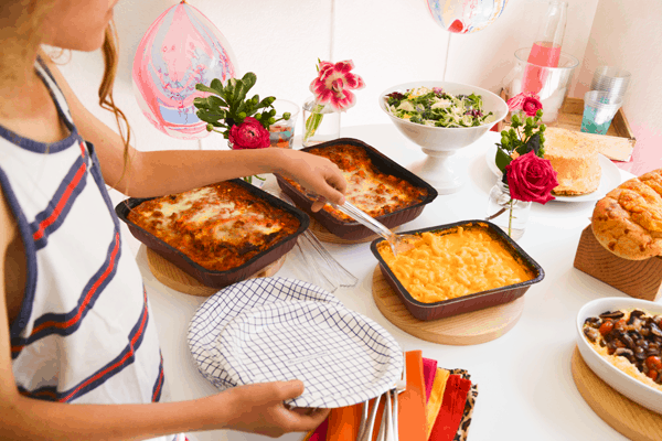 Boy scooping macaroni and cheese on to a plate next to a table of party food for a crowd.