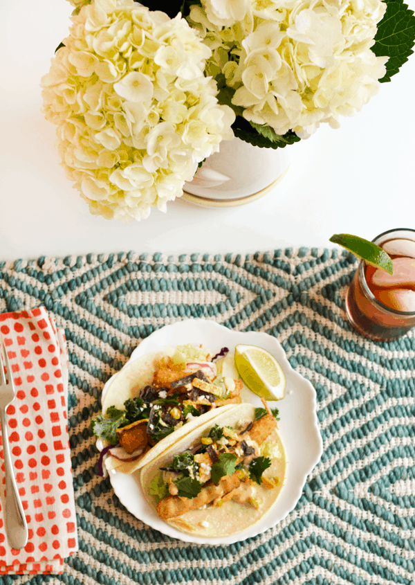 White plate with two fish stick tacos on a woven table mat.