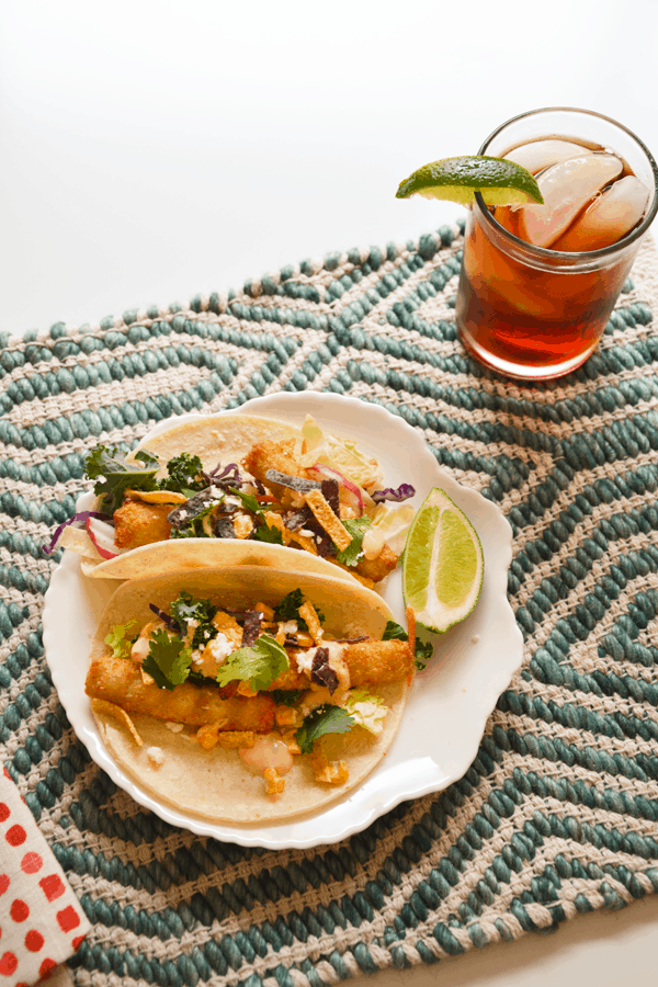 Plate of fish stick tacos next to a glass of coke with ice and lime wedges.