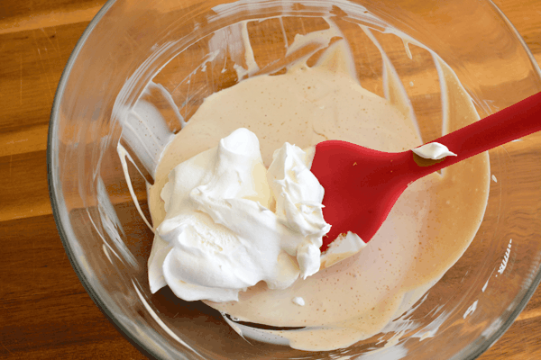 A glass mixing bowl and spatula as whipped topping is being folded into a strawberries romanoff dip mixture.