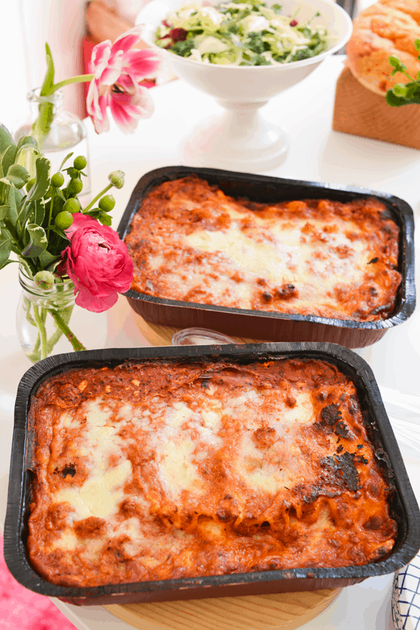 Two large frozen lasagnas on a party table with flowers.