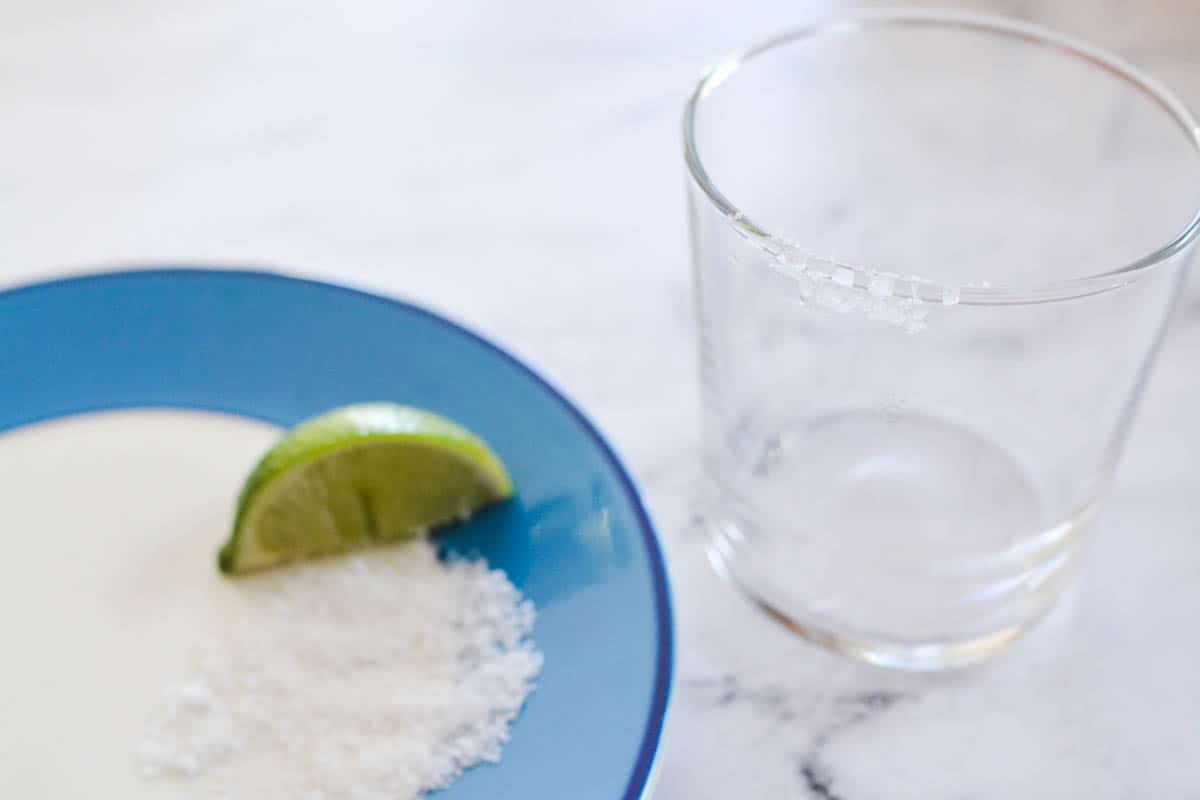 A plate with salt and a piece of lime with a cocktail glass next to it.