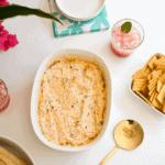 Baking dish with dip on a party table next to crackers and drinks.