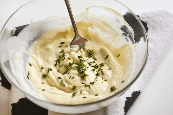 Pizza sauce made with goat cheese, cream and dijon mustard in a glass mixing bowl with a spoon.