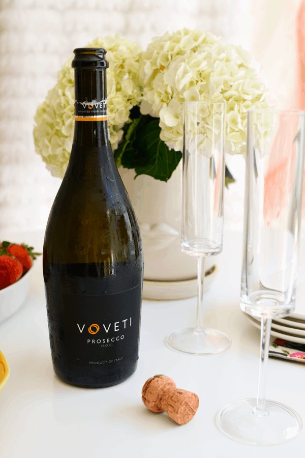 A bottle of Voveti prosecco next to champagne glasses.