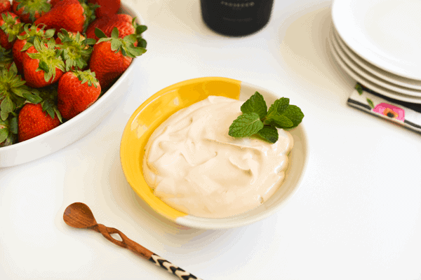 Strawberries romanoff dessert in a yellow and white bowl next to fresh strawberries.