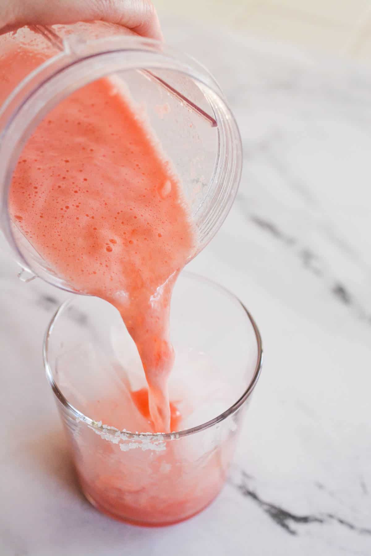 Pouring blended watermelon into a cocktail glass.